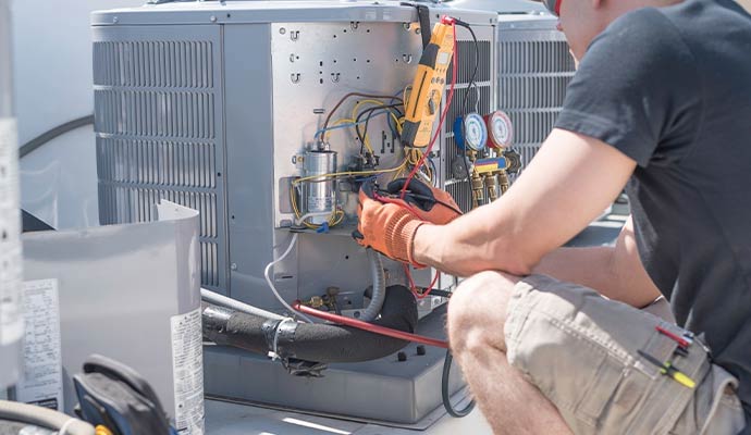 HVAC technician repairing AC unit with multimeter