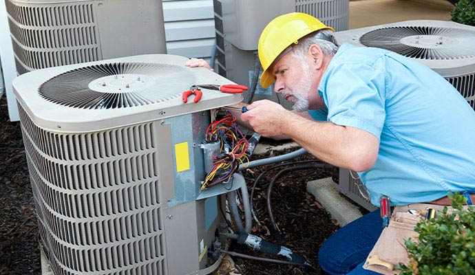 Technician in hard hat repairing outdoor AC unit